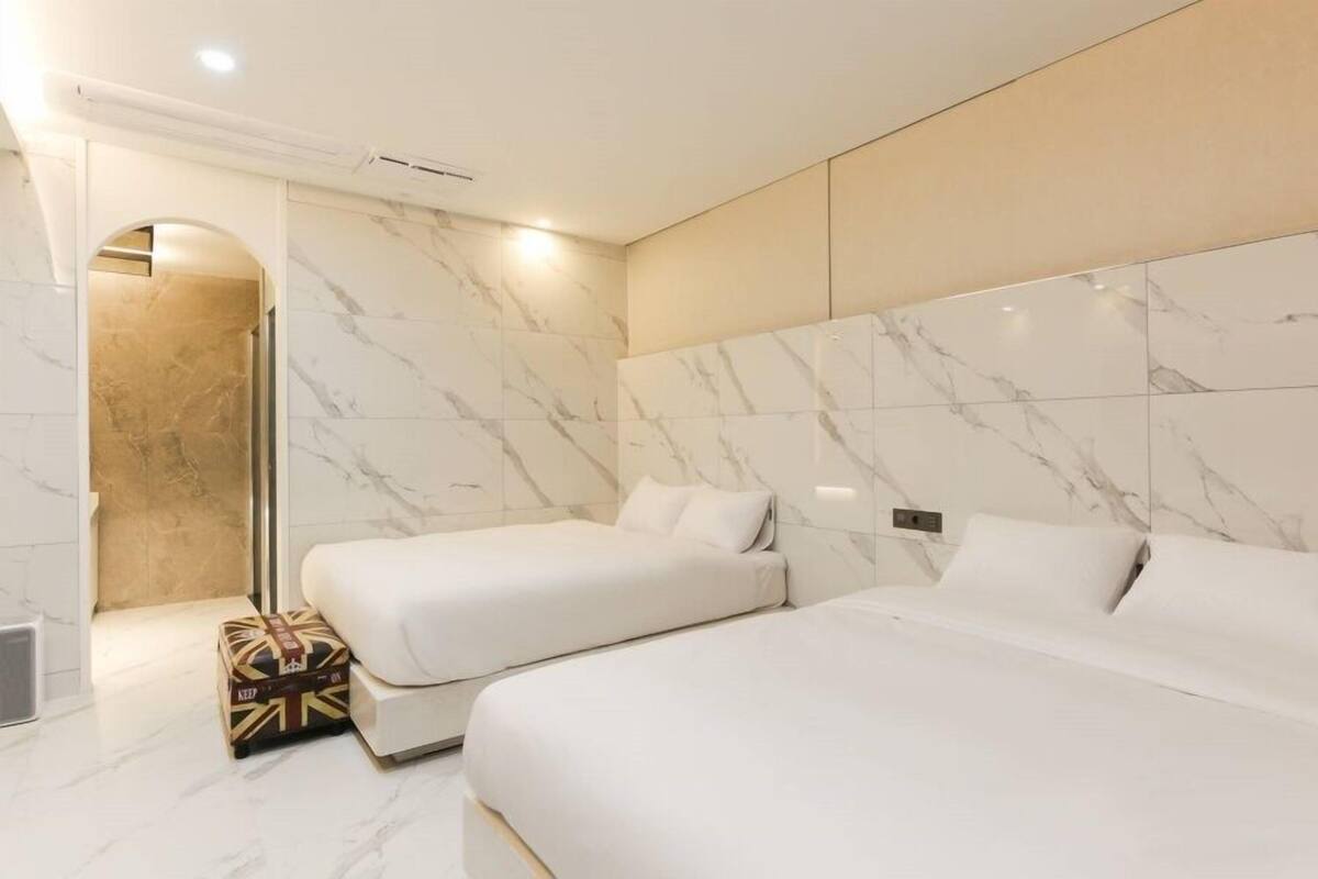 A modern hotel room with two beds, marble walls, and a small luggage storage area.