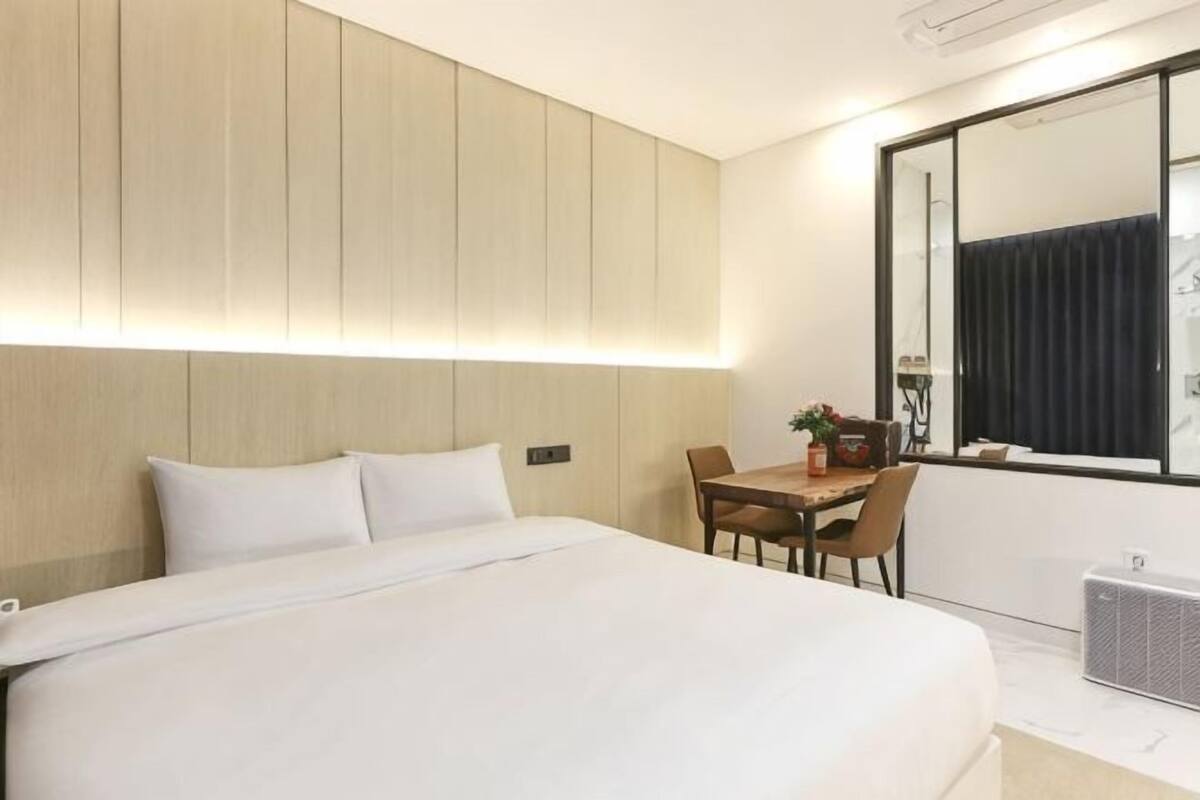 A hotel room with a large bed, a desk with chairs, a small table with a plant, and a large mirror.