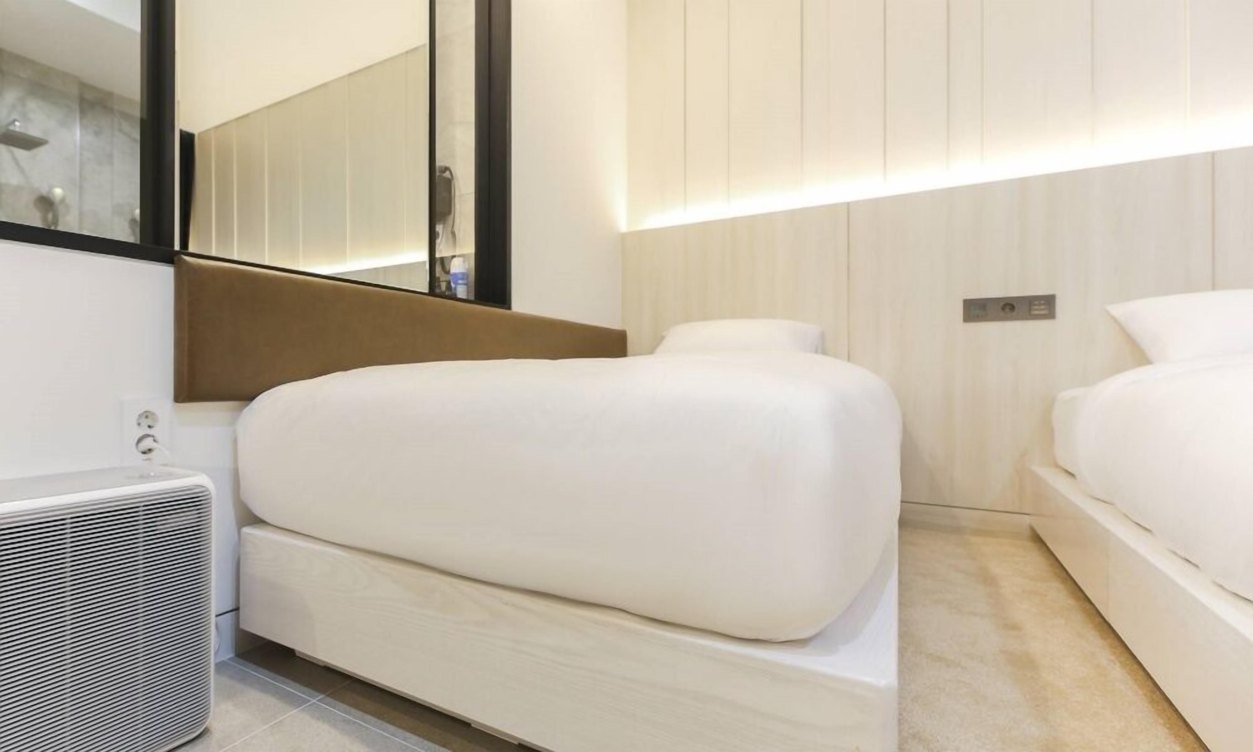 Una habitació d'hotel moderna amb un llit gran, una taula de nit, un mirall i una làmpada de paret.