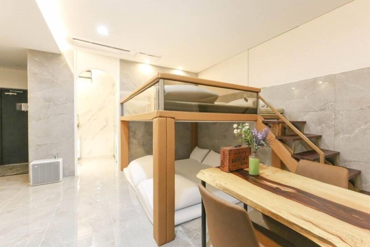 A modern room with a loft bed, a dining table, and a staircase.