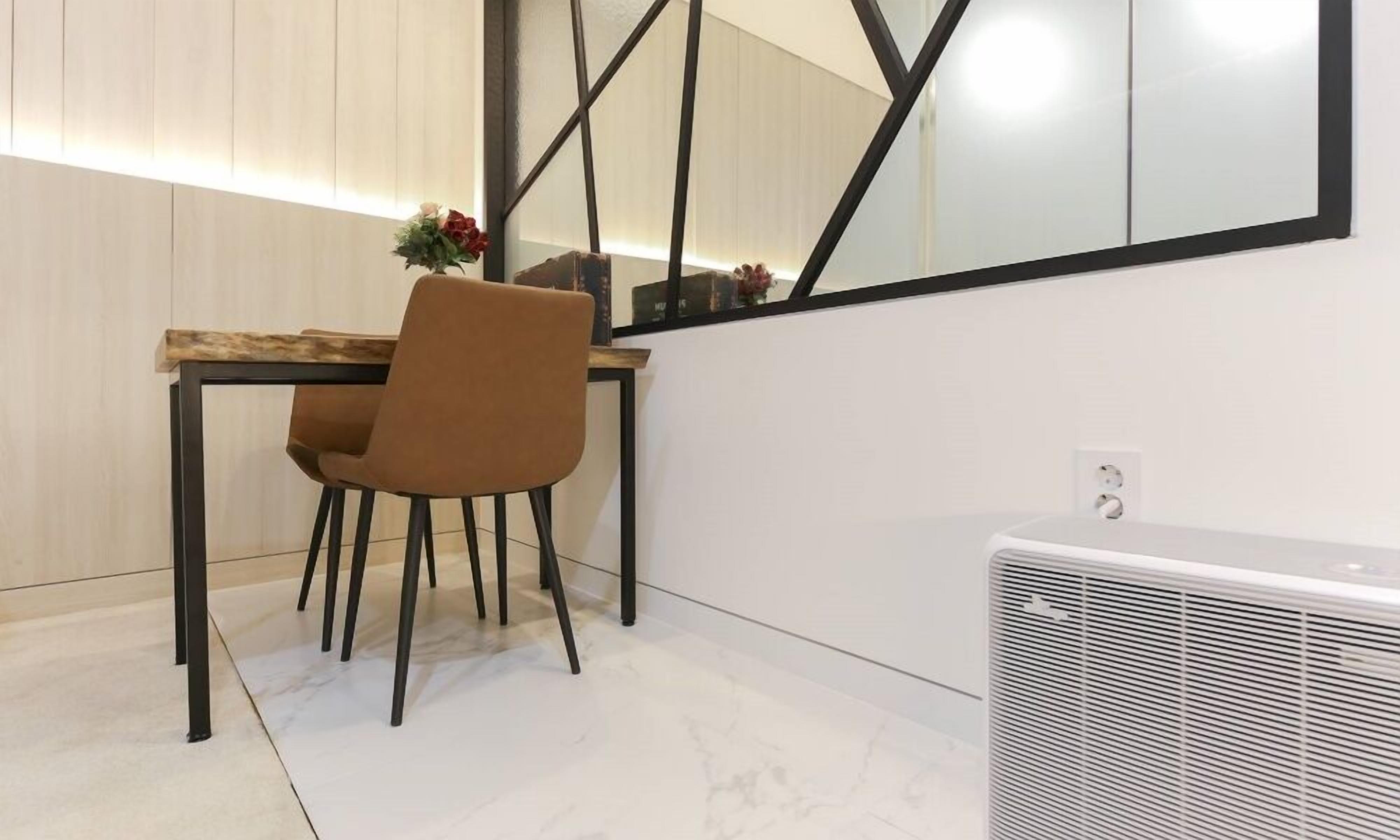 A dining area with a wooden table, a brown chair, a mirror, and a white air conditioning unit.