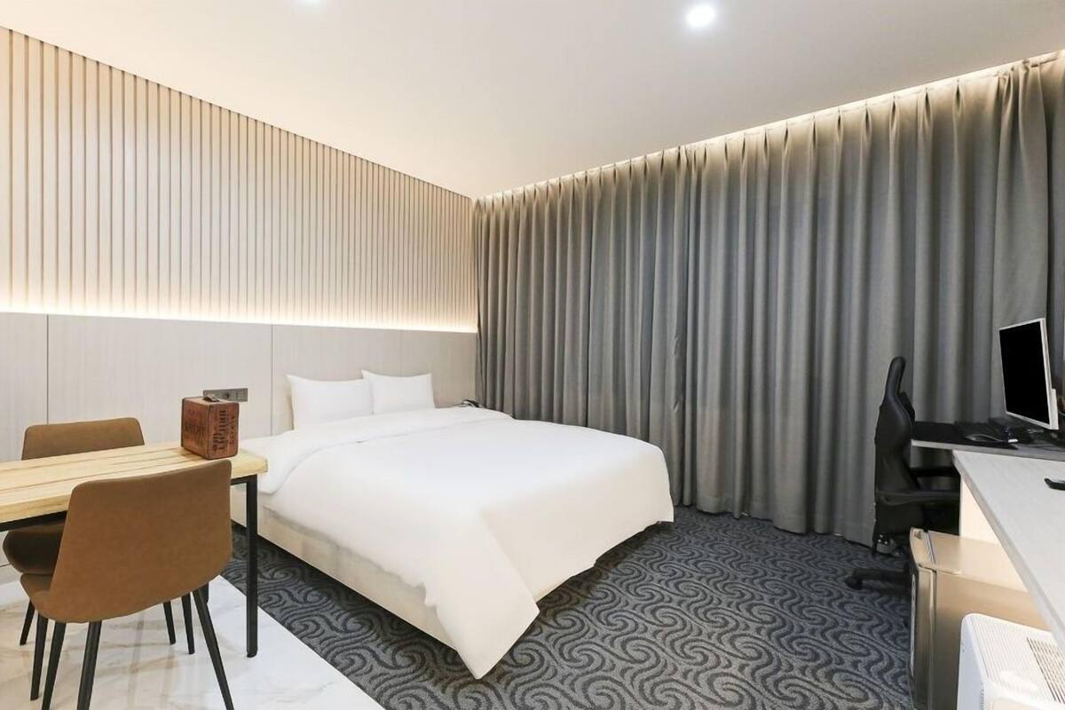 A modern hotel room with a bed, desk, chair, and a computer.