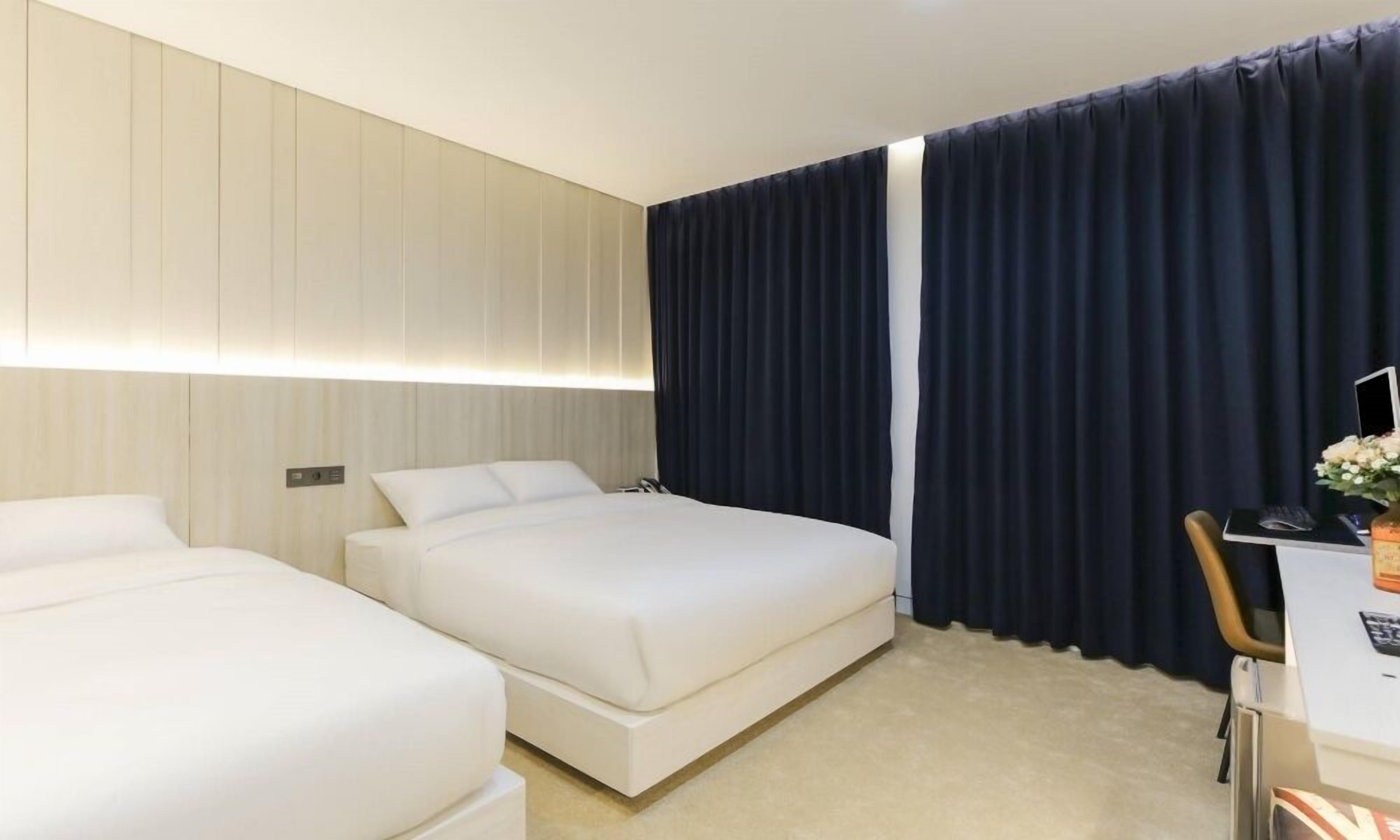 A hotel room with two beds, a desk with a computer, and a dark curtain.