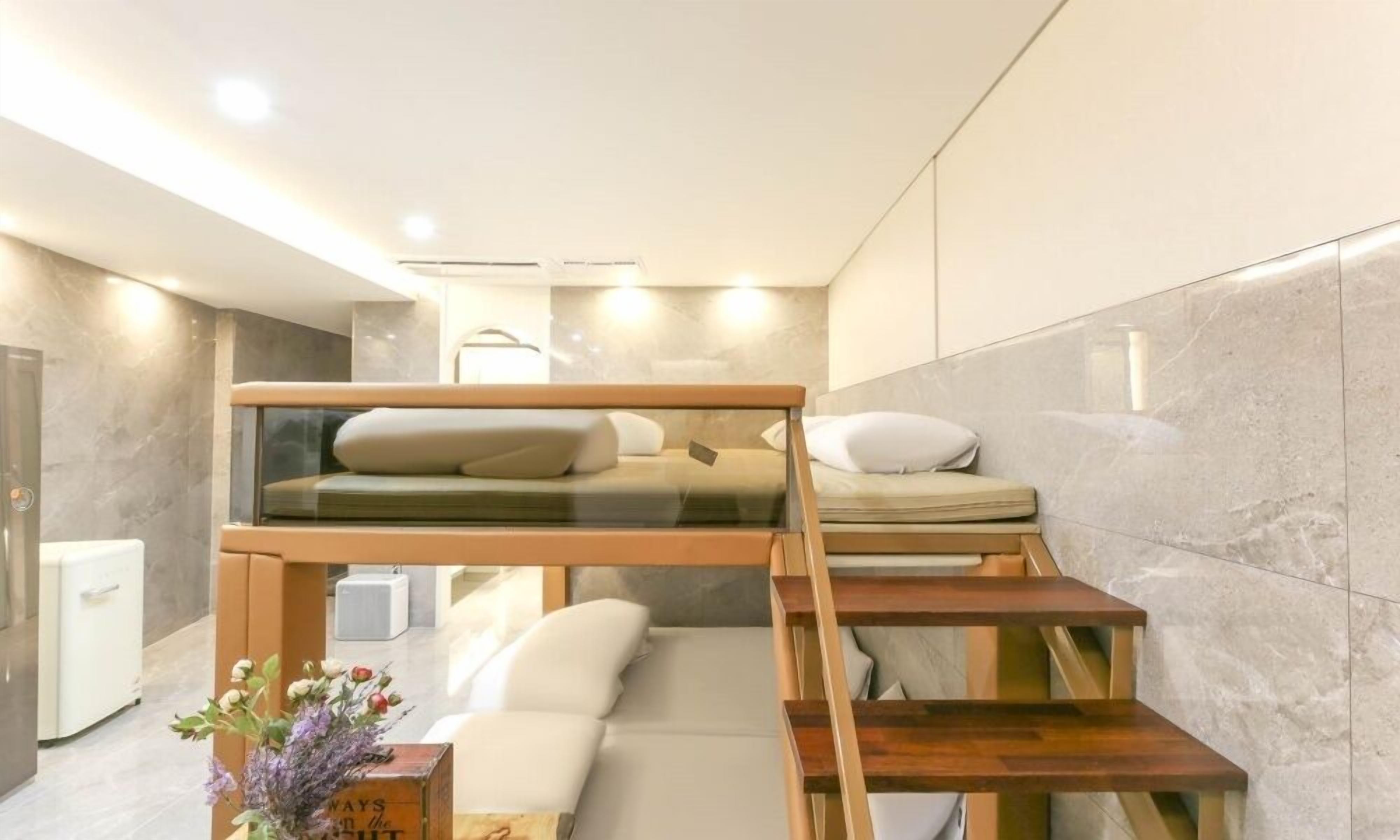 Una habitación moderna y compacta con una litera, un sofá pequeño y una escalera de madera.