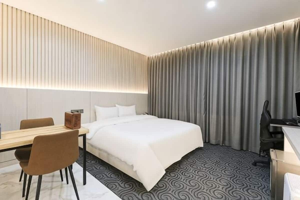A hotel room with a bed, desk, chair, and curtains.