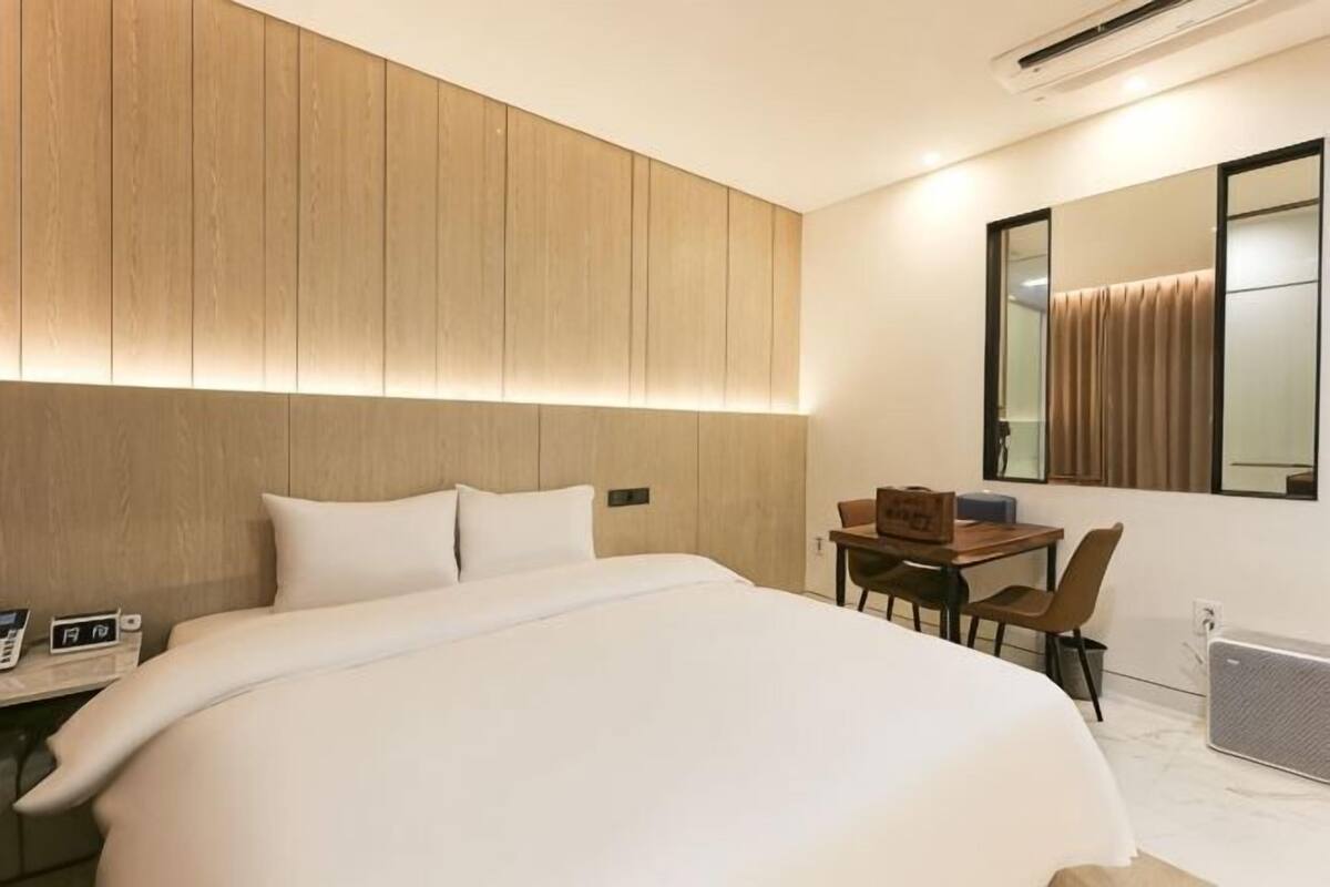 A modern hotel room with a large bed, a desk with a chair, a mirror, and a radiator.
