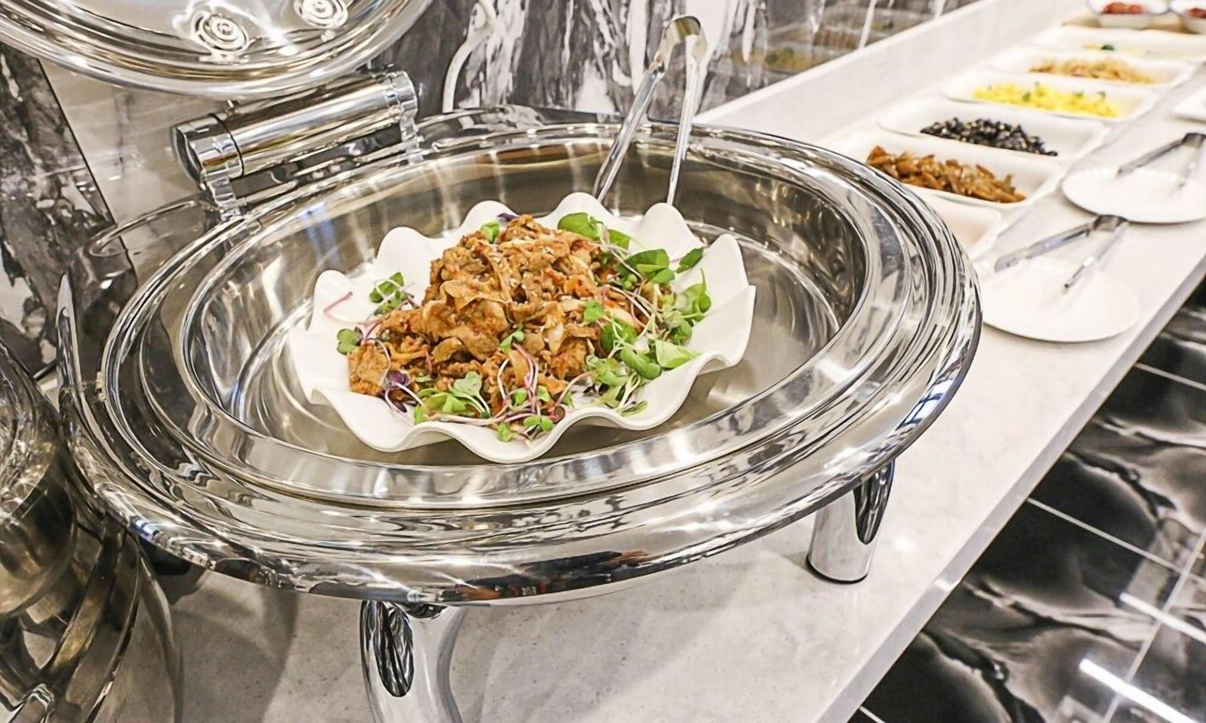 A buffet with a variety of dishes, including a salad with greens and a meat dish, served on a glass platter.