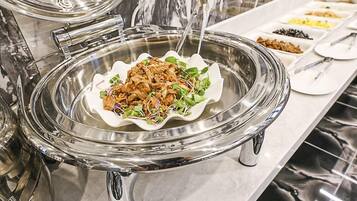 A buffet with a variety of dishes, including a salad with greens and a meat dish, served on a glass platter.