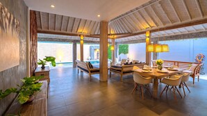 A spacious dining area with a wooden table and chairs, a bench, and a view of a swimming pool. - Villa Bella Vista by Pertama Stay (Seminyak)