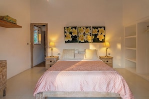 Een slaapkamer met een bed, twee nachtkastjes, een wanddecoratie en een deur die leidt naar een andere kamer.