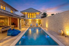 A swimming pool with a deck, a lounge area with chairs, and a house with a balcony. - Villa Bella Vista by Pertama Stay (Seminyak)