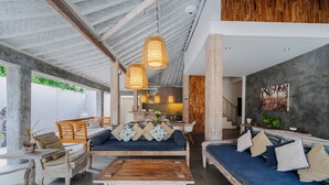 A spacious living area with a high ceiling, wooden beams, and a mix of seating options including sofas and a coffee table. - Villa Bella Vista by Pertama Stay (Seminyak)
