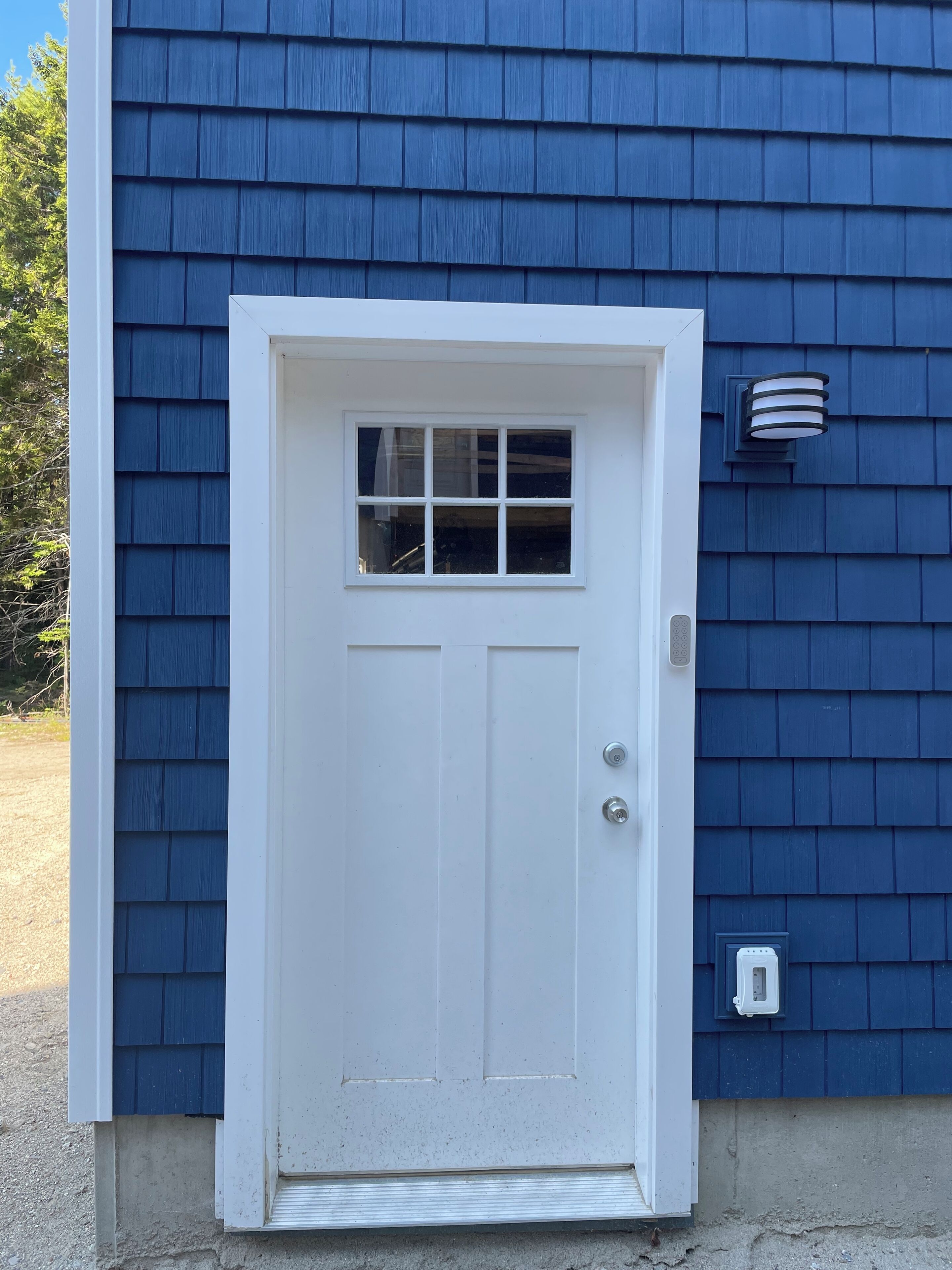 Una puerta blanca con un pequeño ventanal, ubicada en una casa con revestimiento azul.