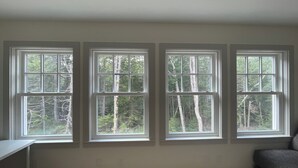 A room with three large windows offering a view of a forest. - Blue Hill in the Woods (Blue Hill)
