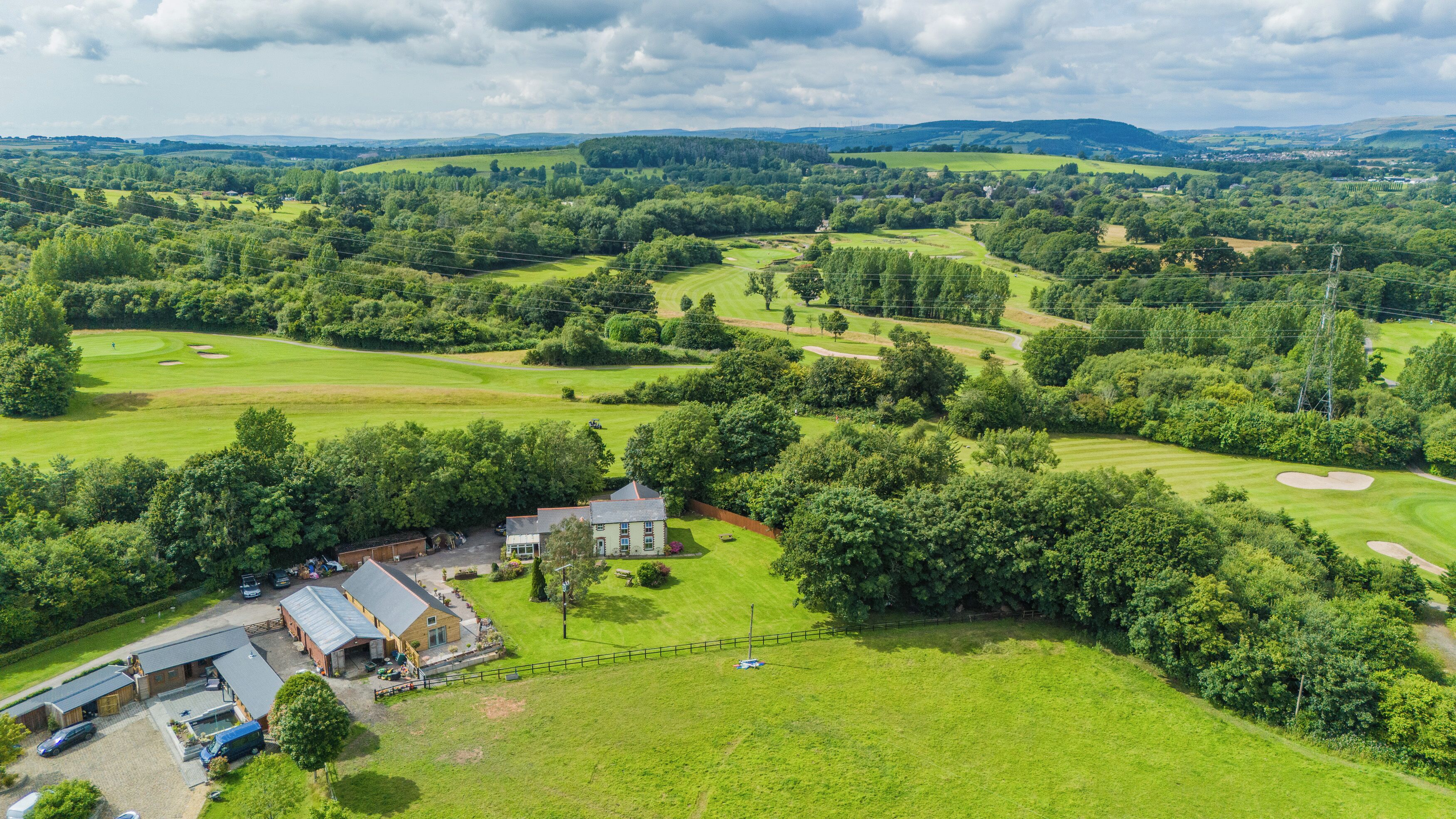 Vue aérienne d’un terrain de golf avec un club-house, un parking et la végétation environnante.