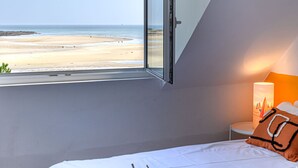 Un dormitorio con vista a la playa, una cama con una bandeja de tazas y una lámpara.