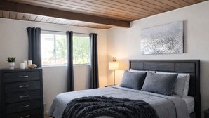 A bedroom with a bed, a dresser, a lamp, and a window with curtains.