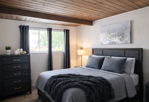 A bedroom with a bed, a dresser, a lamp, and a window with curtains.
