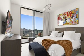 Ein modernes Hotelzimmer mit einem großen Bett, Blick auf die Stadt, einem Bild an der Wand und einem Fernseher auf dem Schreibtisch.
