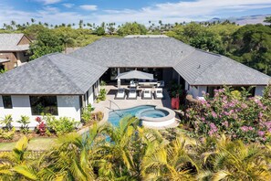 A modern house with a large swimming pool, outdoor seating area, and lush greenery.