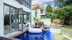 A modern house with a swimming pool, a unicorn float, and a lounge chair.