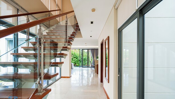 A modern interior with a glass staircase, a hallway leading to a door, and a large window.