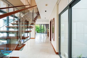 Een modern interieur met een glazen trap, een gang naar een deur en een groot raam.
