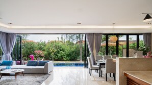A spacious living area with a pool, modern furniture, and large windows offering a view of greenery and buildings.