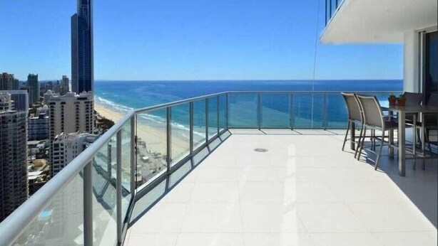 Un balcon doté d’une rambarde en verre, offrant une vue sur une plage et l’océan.