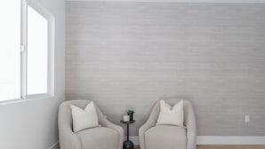A room with two grey armchairs, a small round table with a plant, and a grey textured wall.