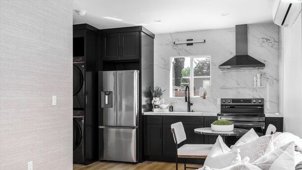 A modern kitchen with dark cabinetry, stainless steel appliances, and a marble backsplash.
