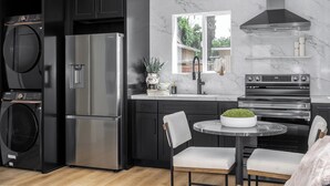 A modern kitchen with a built-in washer and dryer, stainless steel appliances, a marble backsplash, and a view of the outdoors through a window.