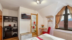 Un dormitorio compacto con cama, una mesita con un florero, una silla, un armario, un microondas y vistas a la montaña a través de una ventana.