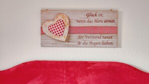 Un letrero de madera con un corazón y texto en una habitación con colcha roja y blanca.