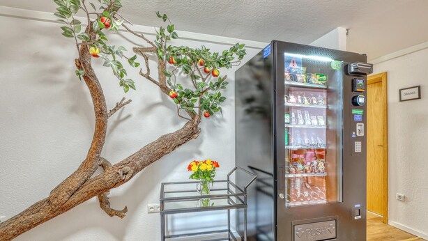 Una máquina expendedora con vitrina de vidrio, una rama decorativa con manzanas, y un jarrón con flores.