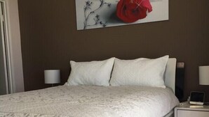 A neatly made bed with a white duvet and pillows, a bedside table with a lamp, and a wall-mounted artwork of a red rose and black silhouette. - Expansive Ocean Views from Peninsula (Surfers Paradise)