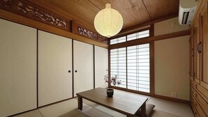 Une pièce traditionnelle japonaise avec un sol recouvert de tatamis, des portes coulissantes en papier de riz (shoji), une petite table basse et une lanterne en papier suspendue.