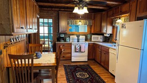 A wooden kitchen with a dining table, chairs, a stove, a microwave, and a refrigerator.