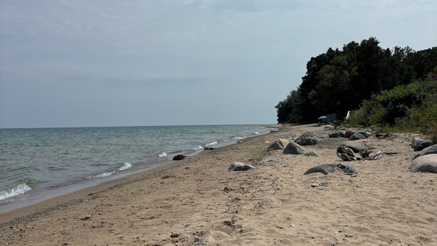 A sandy beach with scattered rocks and a calm sea.