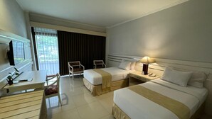 A hotel room with two beds, a desk, a chair, a lamp, and a window with curtains. - Queen Garden Hotel by Salak Hospitality (Baturaden)