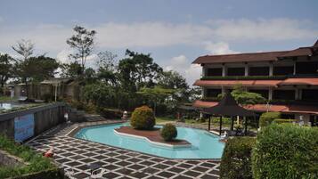 Relax by the rectangular pool surrounded by lounge chairs and umbrellas, set amidst lush greenery and trees.