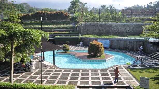 A swimming pool with a tiled deck, surrounded by greenery and a stone wall. - Queen Garden Hotel by Salak Hospitality (Baturaden)