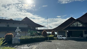 A hotel entrance with a statue, a sign reading "Queen Hotel," and a parked car. - Queen Garden Hotel by Salak Hospitality (Baturaden)