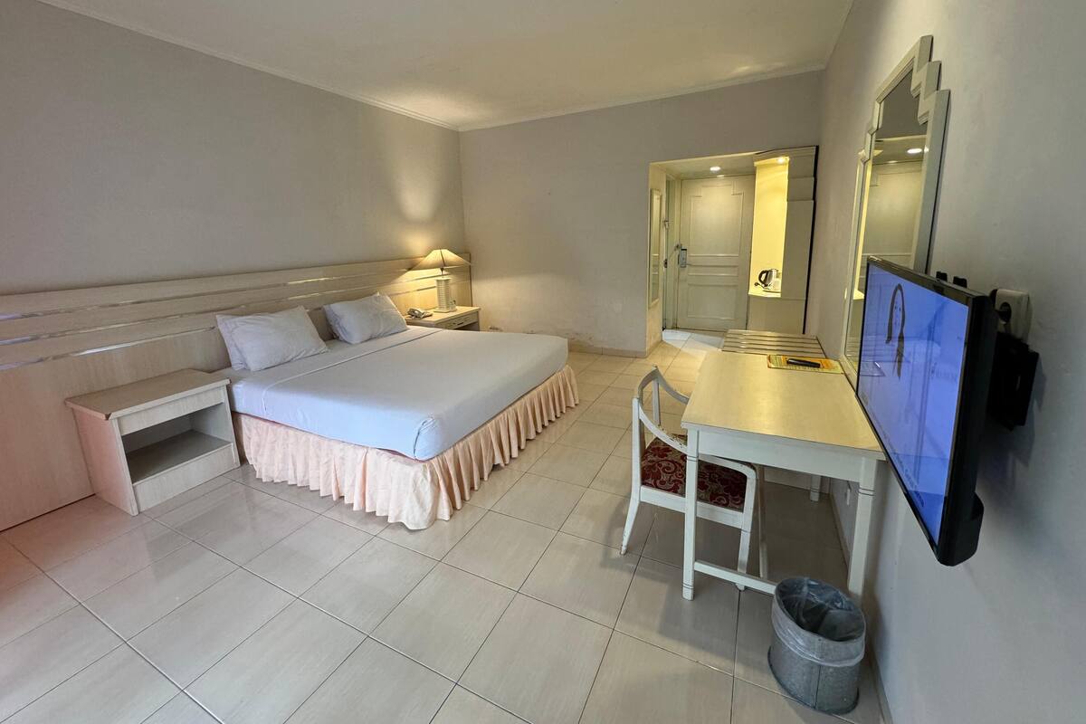 Une chambre d’hôtel comprenant un lit, une table de chevet, une lampe, un bureau, une chaise et un téléviseur.