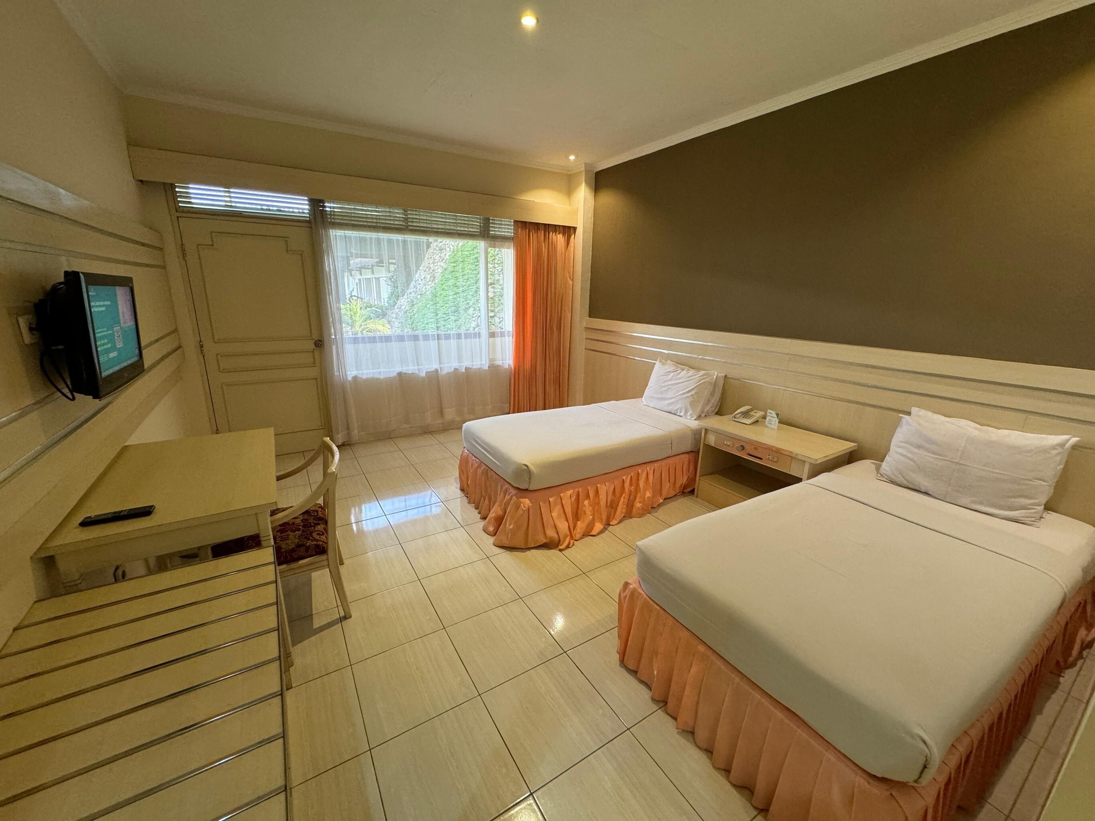 Een hotelkamer met twee bedden, een bureau, een stoel, een televisie en een raam met gordijnen.