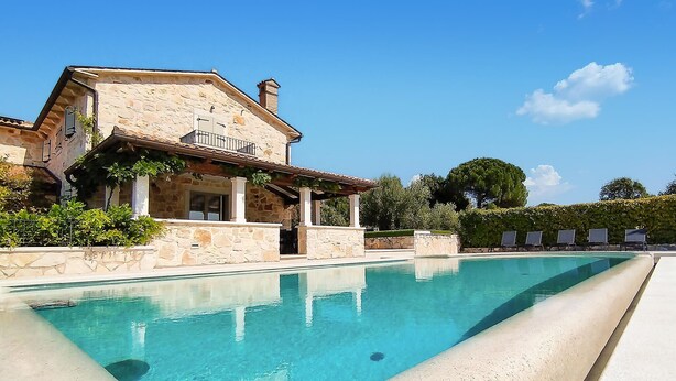 A stone villa with a swimming pool, a covered patio, and a view of the surrounding greenery.