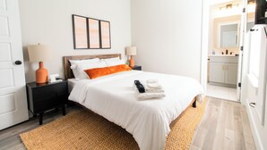 Ein Hotelzimmer mit Bett, Nachttischen, einer Lampe, einem Teppich und einem durchgegangenen Tür sichtbaren Badezimmer.