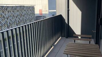 A balcony with a metal railing, two wooden benches, and a view of a building with a red sign.