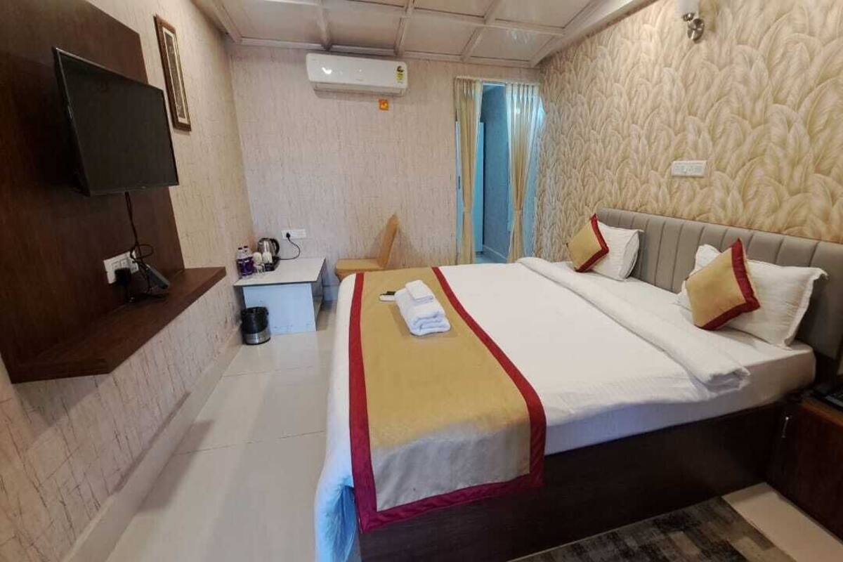 Habitación de hotel con cama, mesita de noche, televisión y un pequeño escritorio con silla.