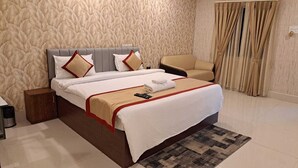 A hotel room with a large bed, a chair, a nightstand, and a patterned wall.